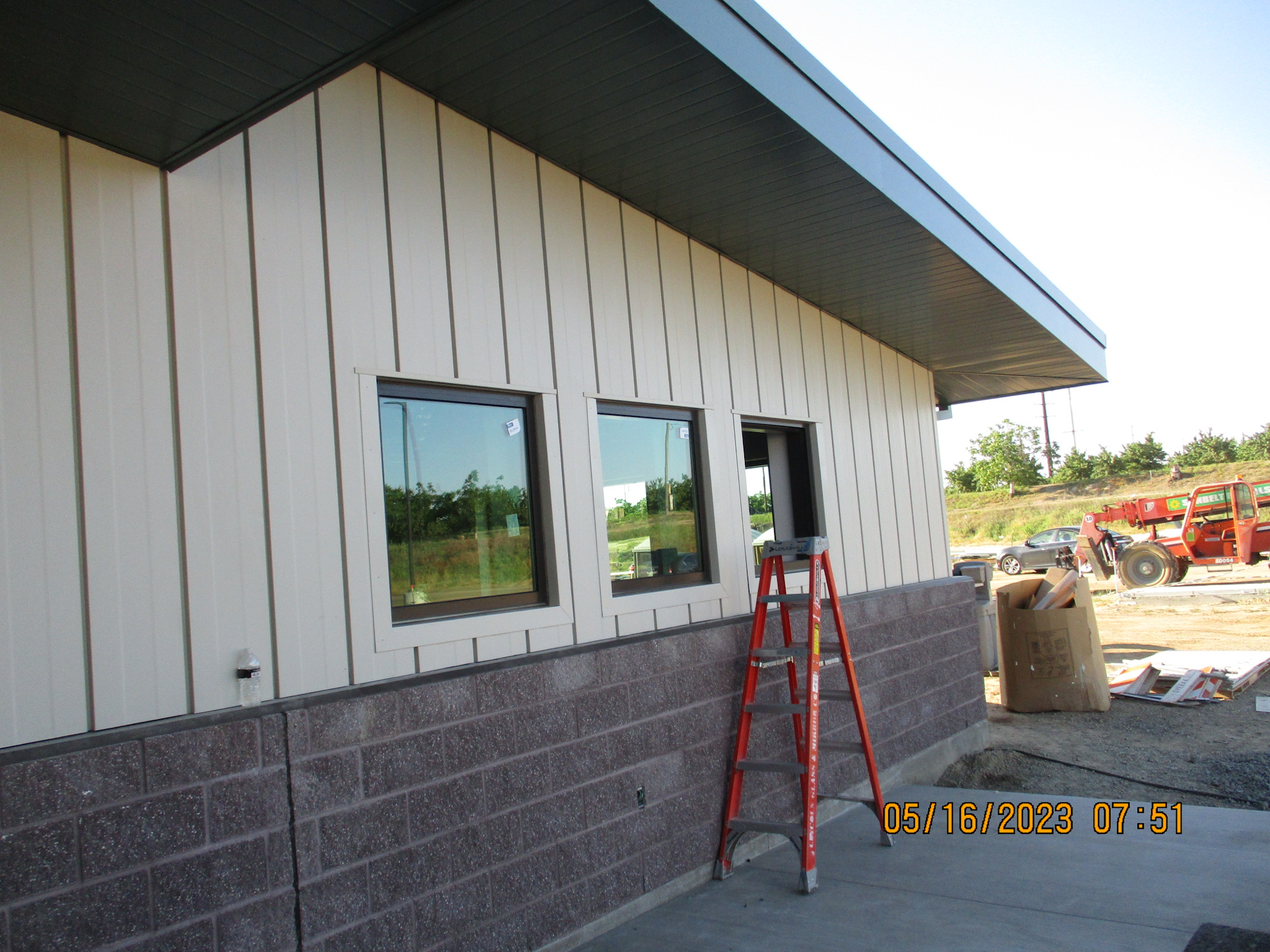An industrial building with windows, an orange ladder, construction debris, and a forklift in the background.