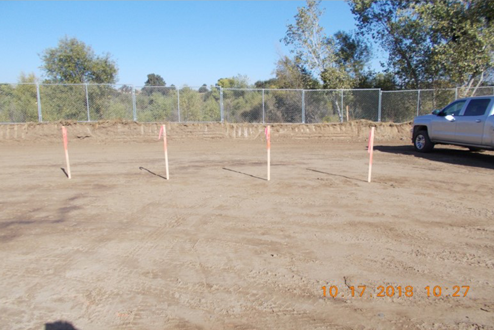 A fenced dirt lot with marked stakes and a truck.