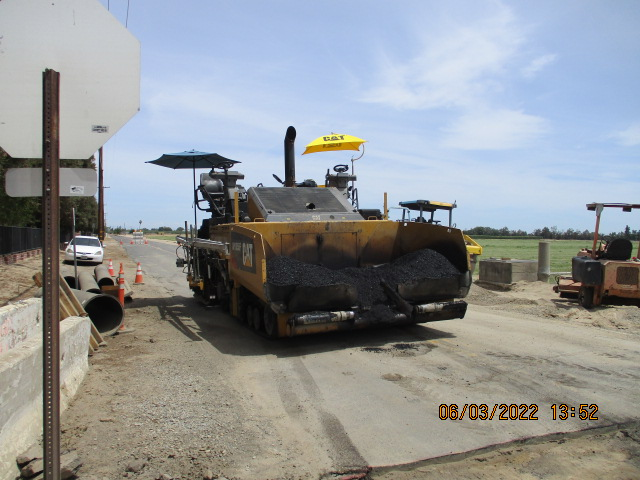 A yellow asphalt paver on a road construction site with clear skies and a date stamp.