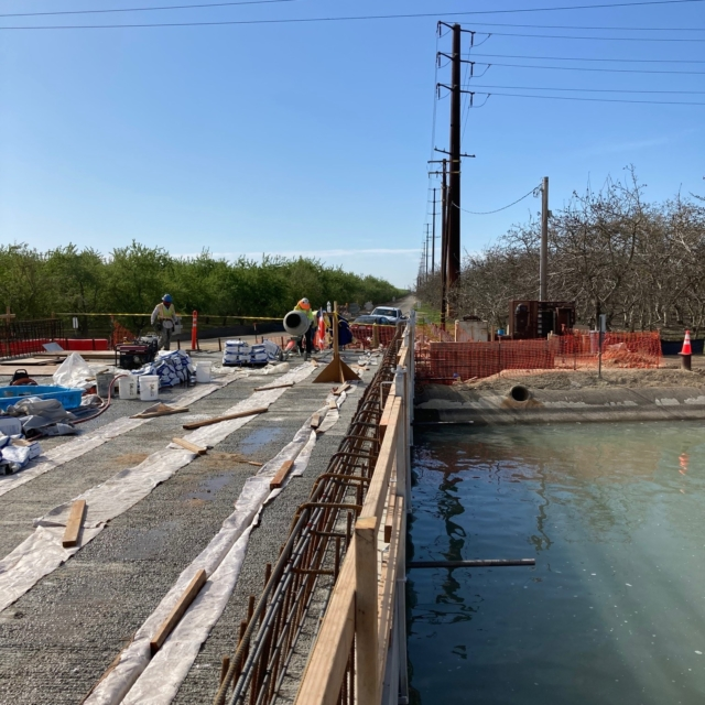 Construction site with workers, materials, and concrete forms near water.
