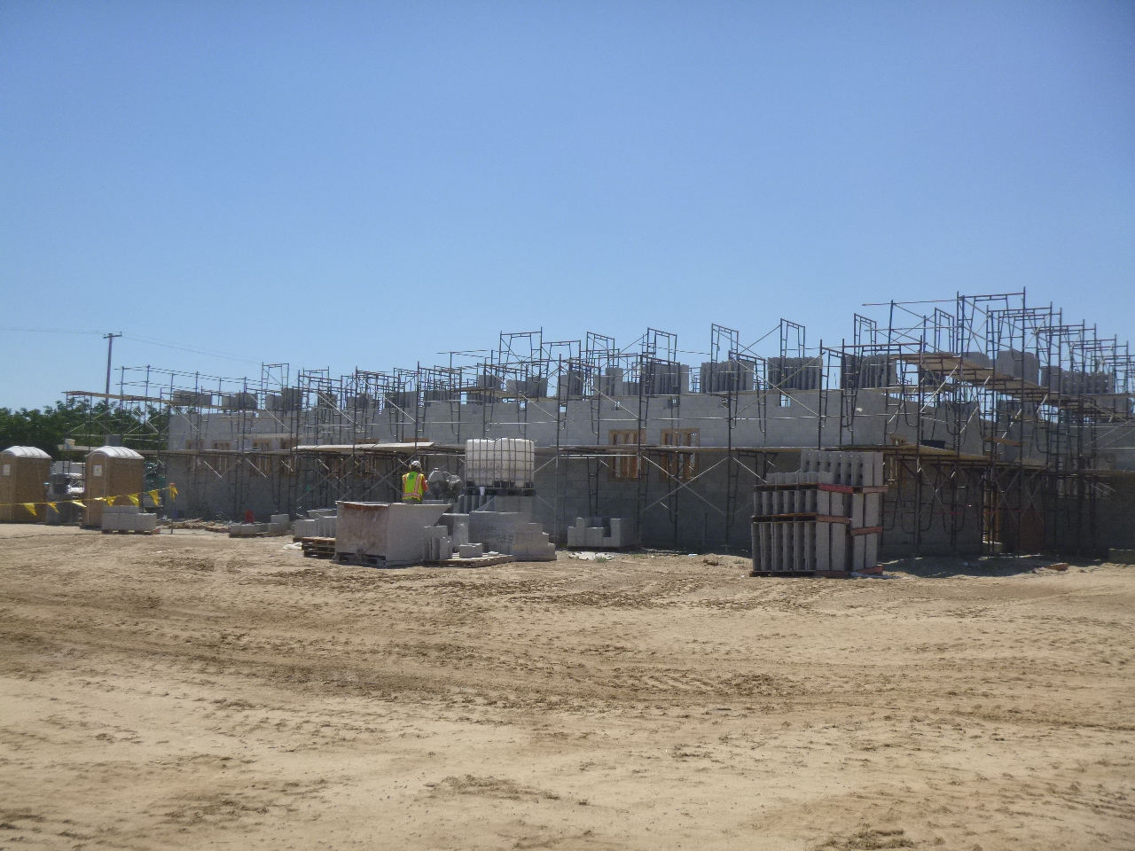 A construction site with scaffolding, building materials, and a worker in high-visibility clothing.