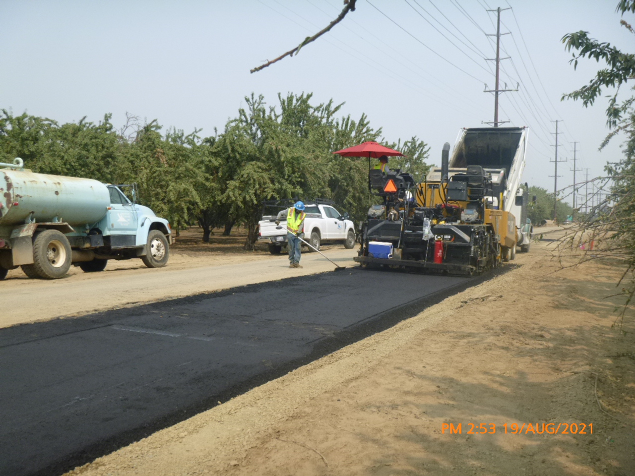 Road construction with machinery and workers laying asphalt.