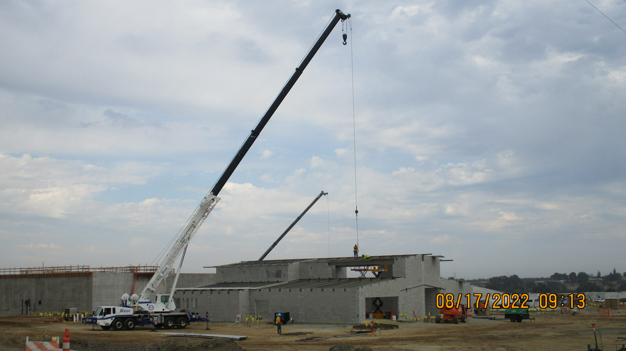 A construction site with cranes lifting materials, under a cloudy sky.