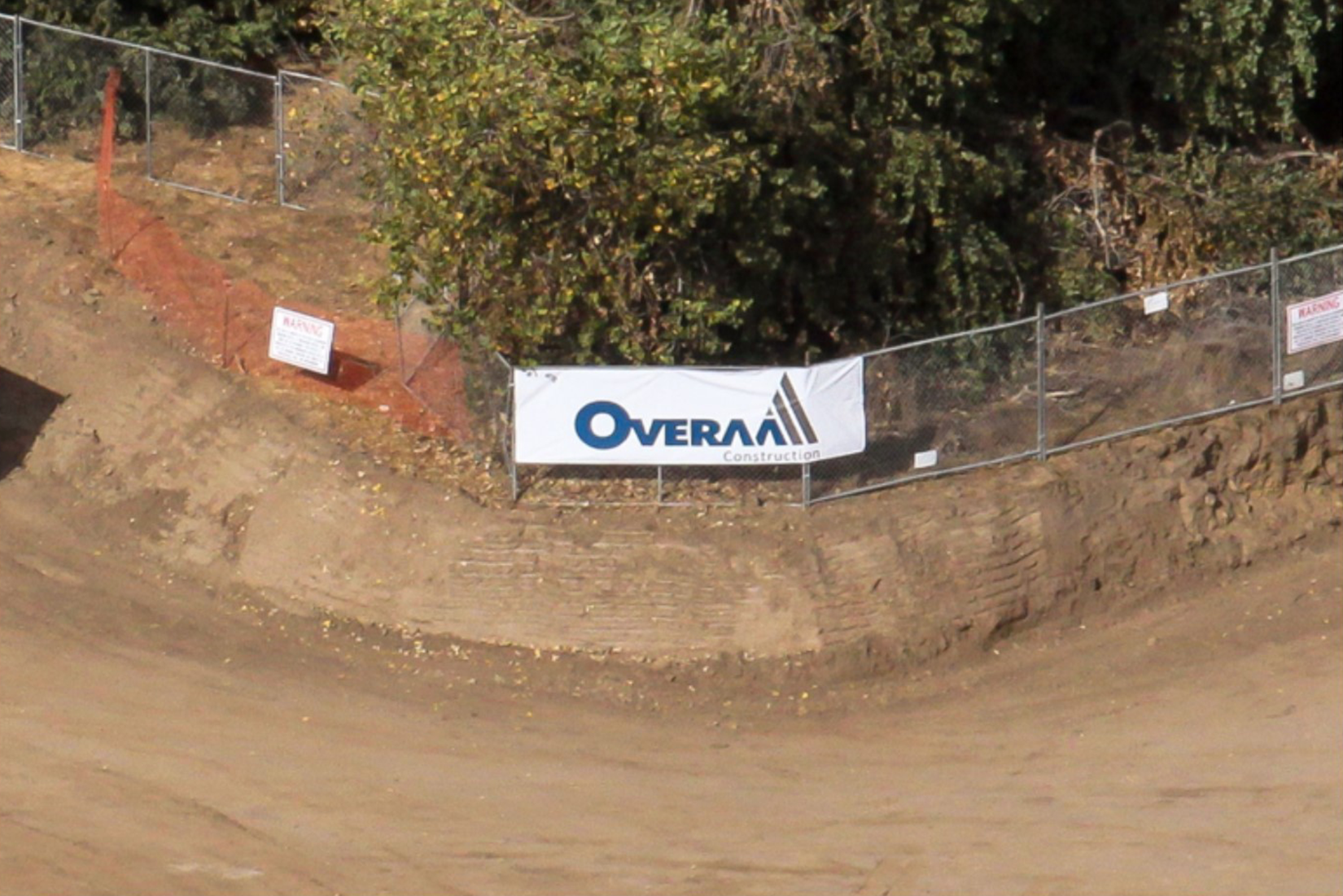 A construction site with a banner displaying the name "Overall Construction," fencing, and earthwork.