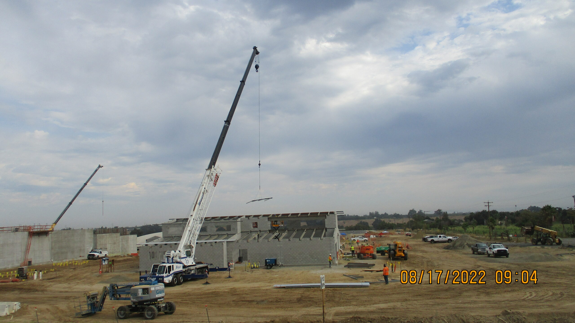 Construction site with cranes, vehicles, and workers under a cloudy sky.