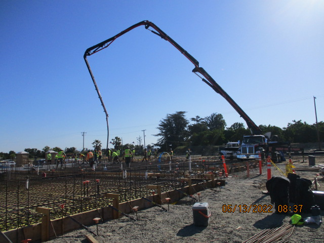 Construction site with workers, a concrete pump truck, and reinforcement bars.