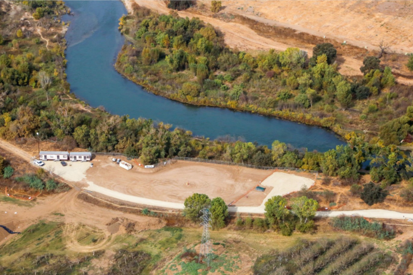 Aerial view of a river bend with adjacent construction site and temporary buildings.