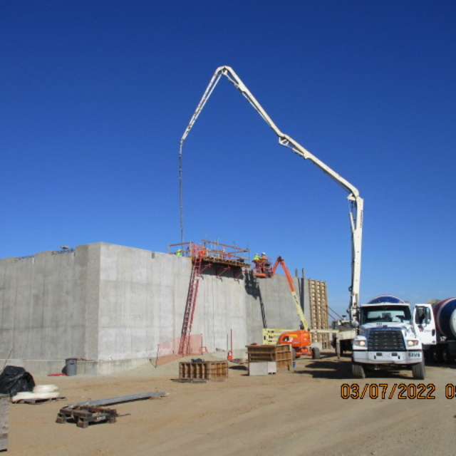 Concrete pump truck extending boom over construction site with clear blue sky.