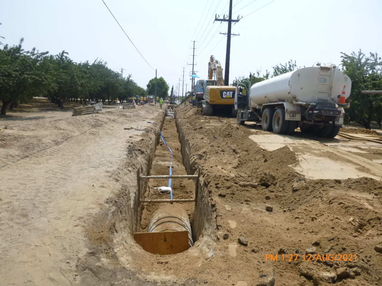 Roadwork with a trench and construction machinery, near an orchard.