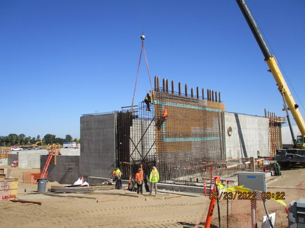 Construction site with crane, workers, and concrete walls.