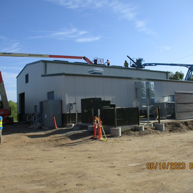 Construction site with workers on a lift, industrial building, and equipment.