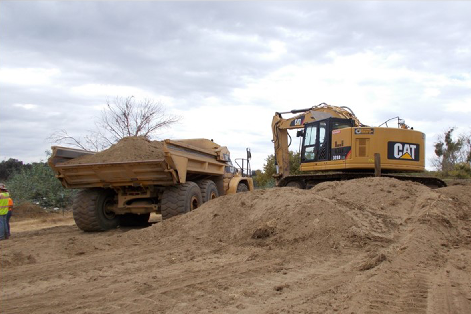 Construction site with an excavator, a dump truck, and a person wearing a high-visibility vest.