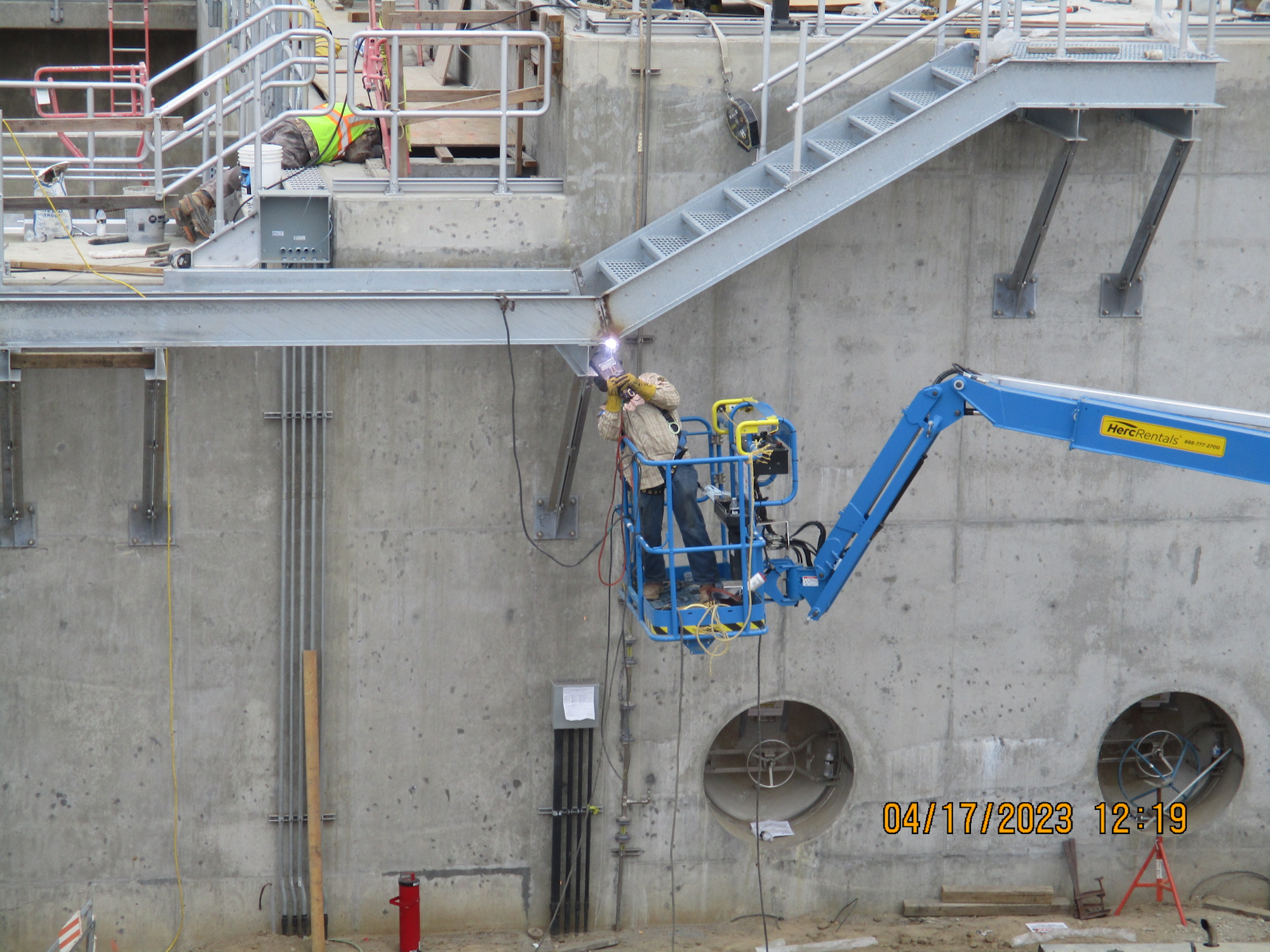 Construction workers on a site with a crane and welding equipment.