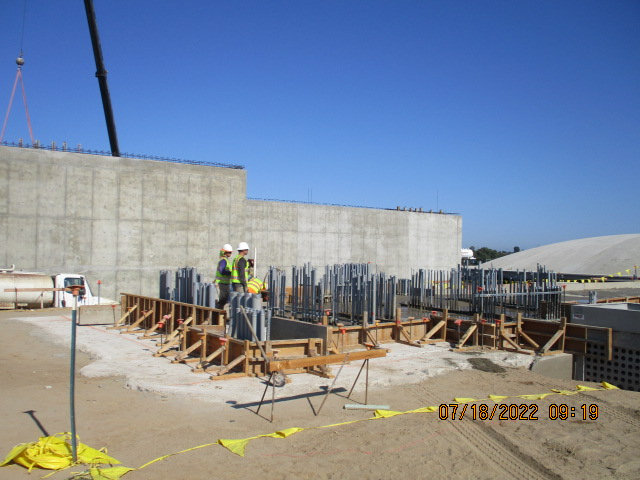 Construction site with two workers, concrete wall, steel reinforcements, and wooden forms.