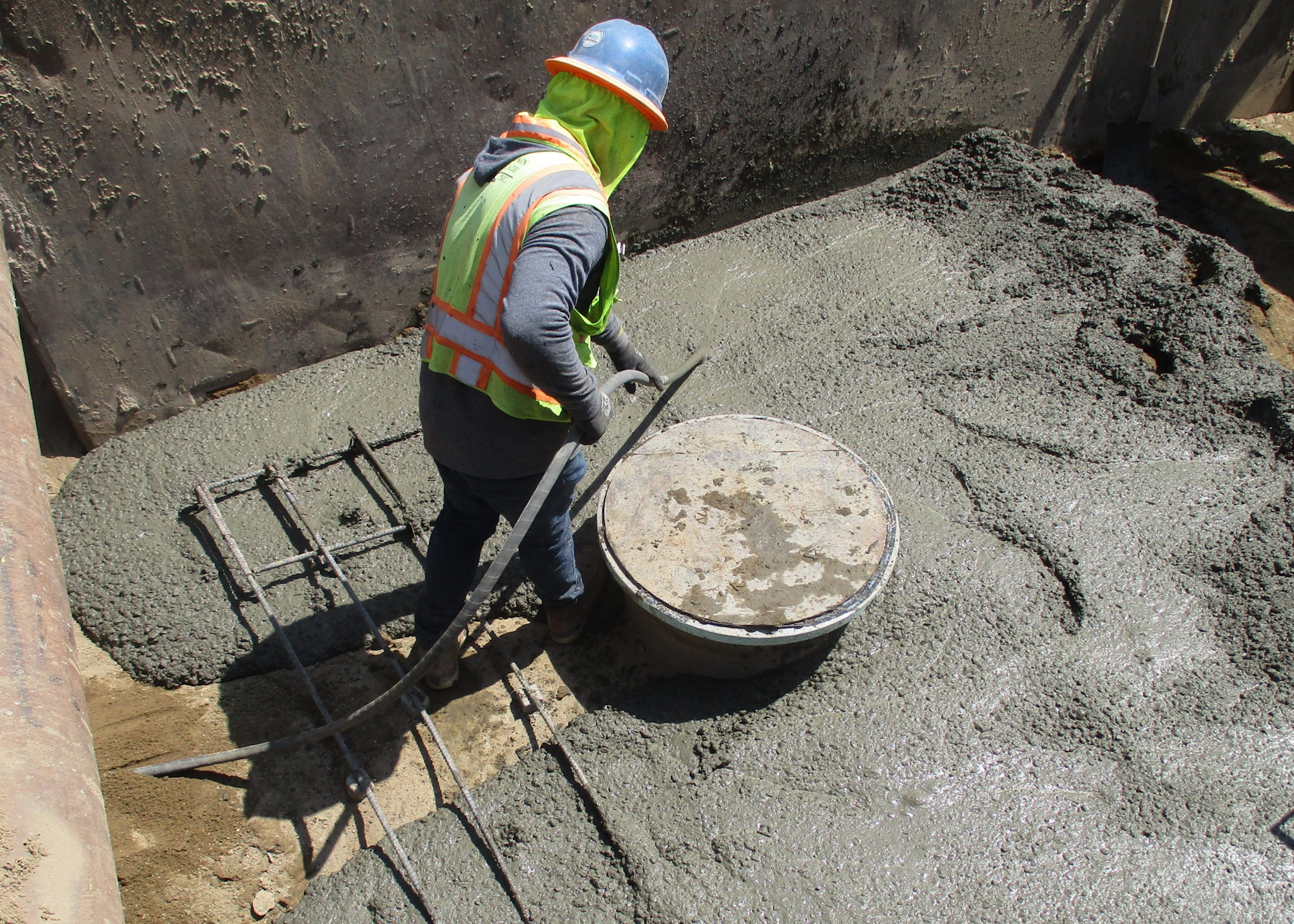 A worker in a high-visibility vest levels wet concrete with tools at a construction site.