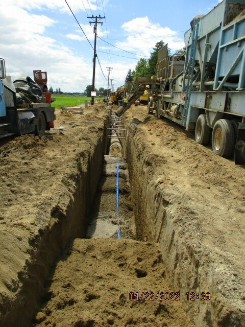 Trench for pipes with construction equipment and vehicles along a dirt road.