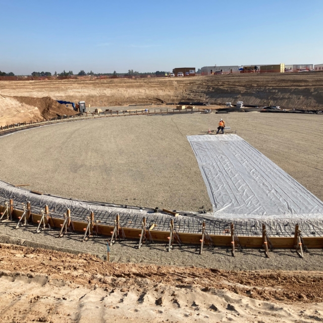 Construction site with excavated ground, gravel layer, and worker unrolling geotextile material.