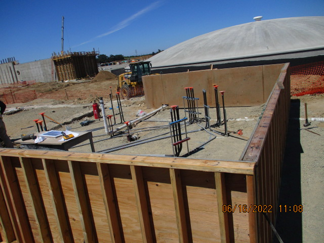 Construction site with wooden formwork, steel rebar, equipment, and partially built concrete structures under a clear sky.