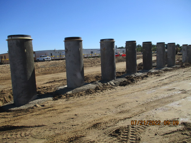 A row of concrete pillars on a construction site with sandy ground and timestamp.
