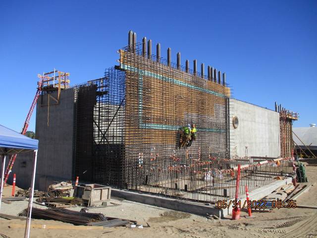 A construction site with workers, reinforcing steel bars, concrete structures, and construction equipment.