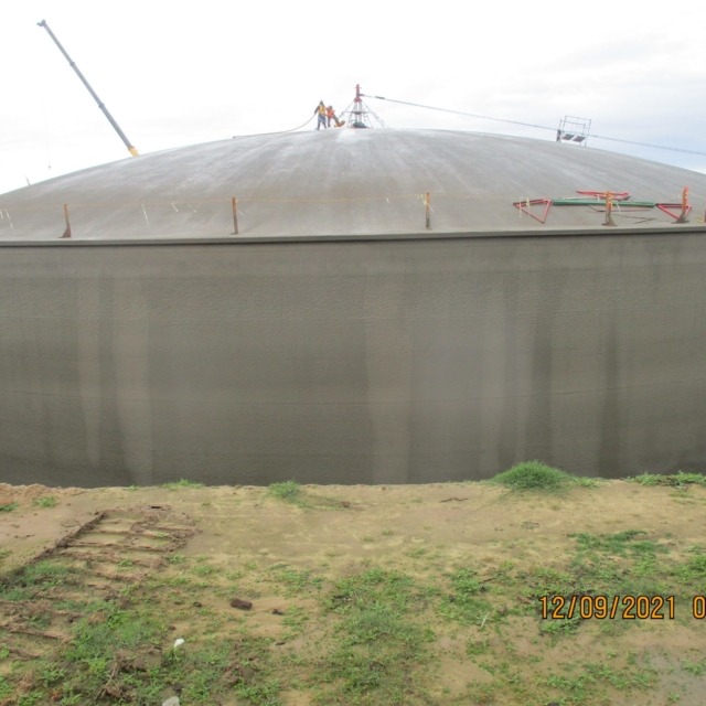 Large storage tank with people on top, crane nearby, cloudy sky, timestamped.