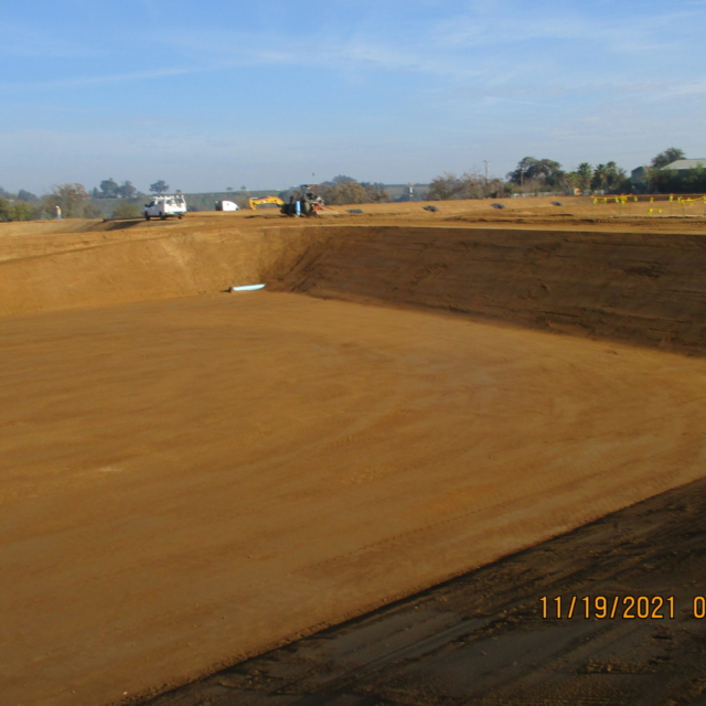 Large construction site with excavated area, heavy machinery in the background, and a clear sky.