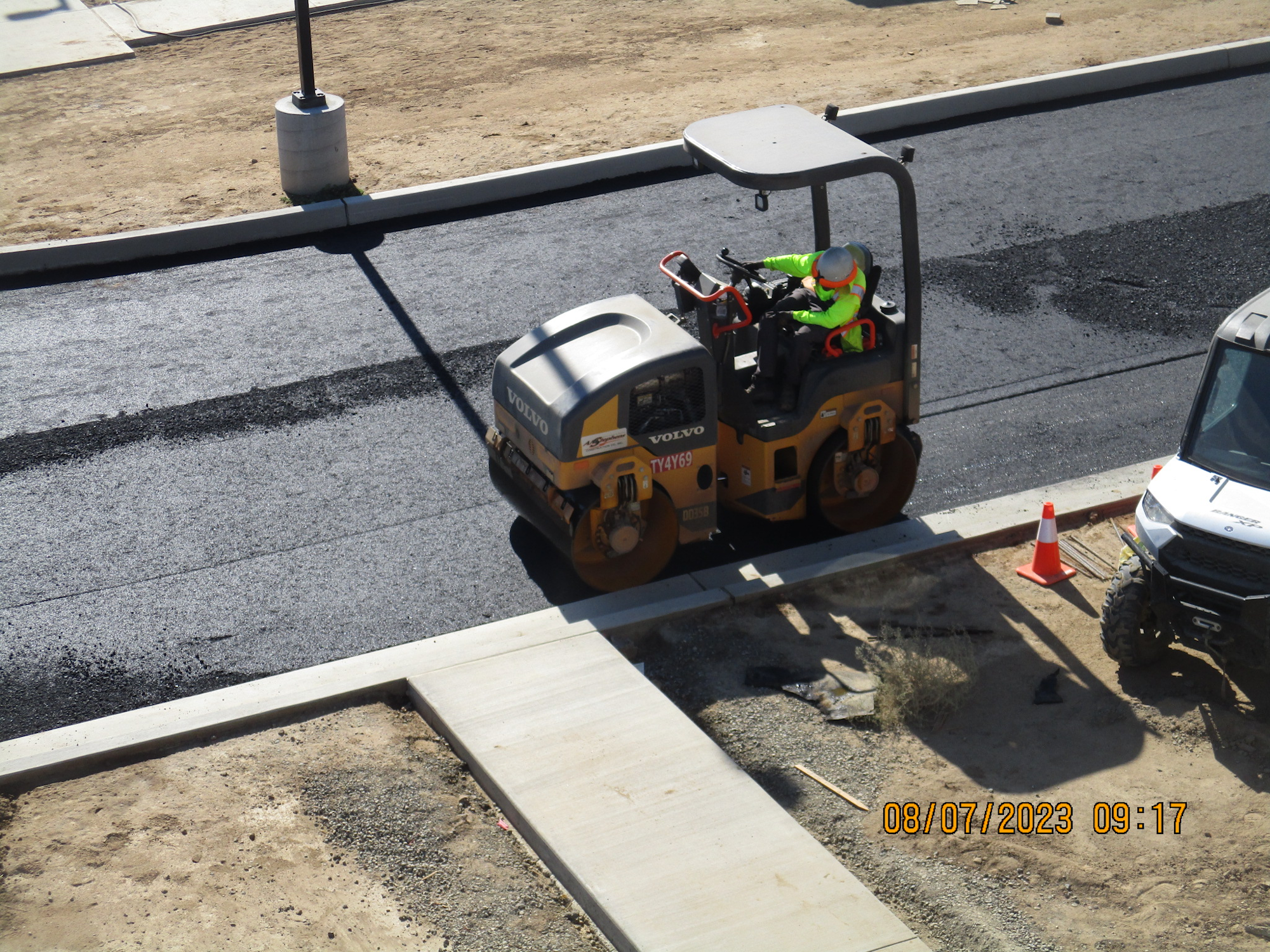 Road construction with a worker operating a roller compactor.