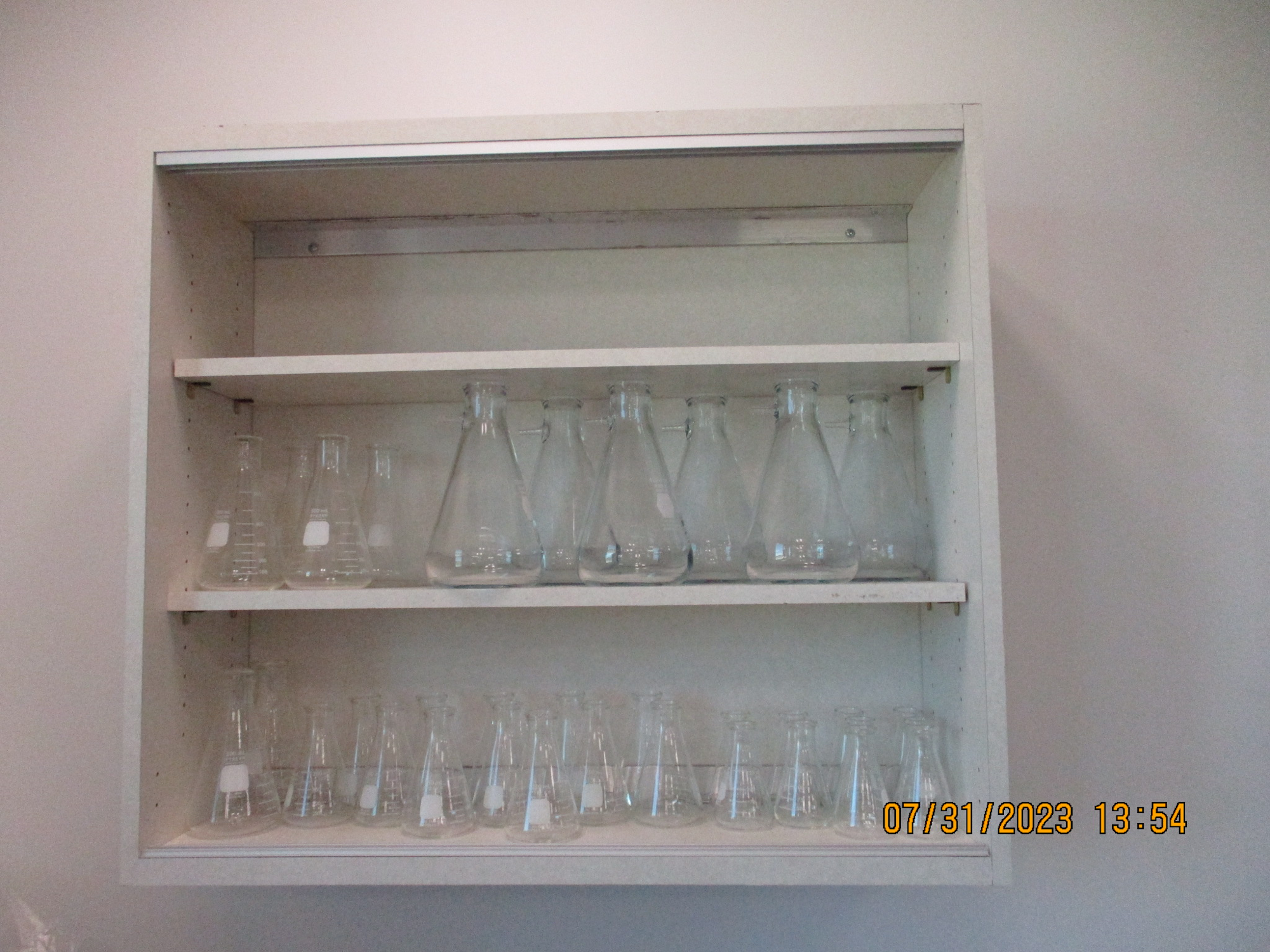 A white shelf with various glass flasks and beakers, suggesting a laboratory setting.