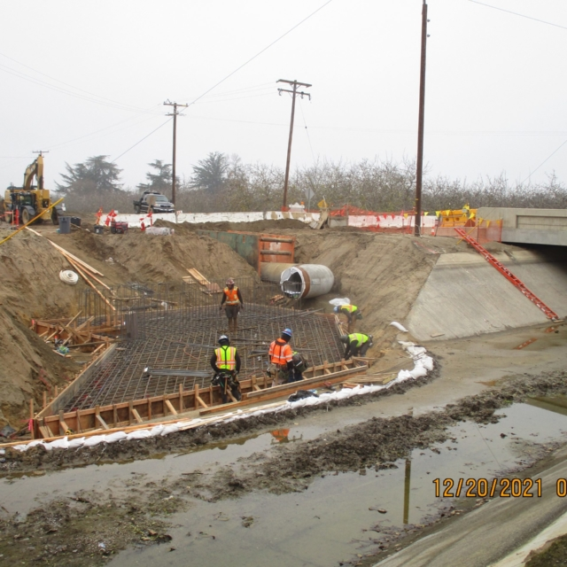 Construction site with workers, concrete culvert, and rebar framework.