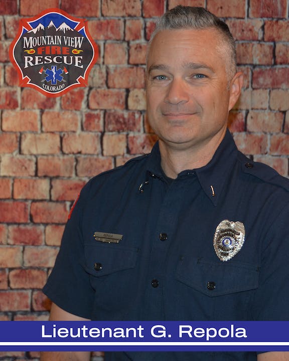 A firefighter in uniform with a badge in front of a brick wall, under a Mountain View Fire Rescue logo.