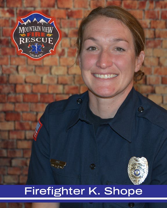 A smiling firefighter in uniform with a badge and a fire and rescue emblem in the background.