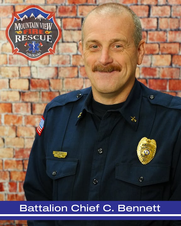 Image of Battalion Chief C. Bennett from Mountain View Fire Rescue, smiling in a navy uniform against a brick wall backdrop.