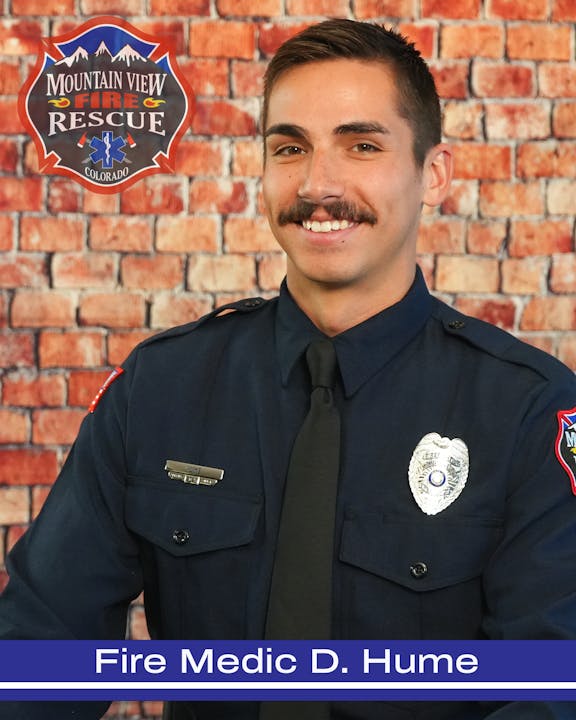 A uniformed fire medic from Mountain View Fire Rescue with a badge and name tag, smiling against a brick wall.