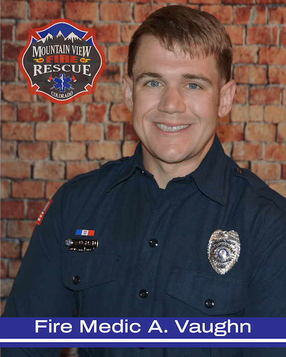A smiling person in a firefighter uniform with a badge, in front of a brick wall, and a fire and rescue service logo for Mountain View, Colorado.
