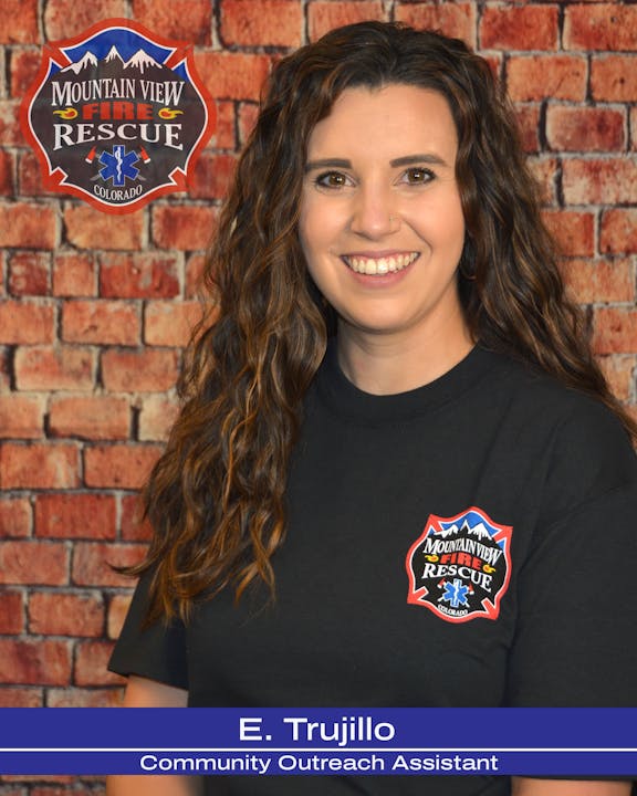 A woman in a black shirt with a Mountain View Fire Rescue logo, standing in front of a brick wall.