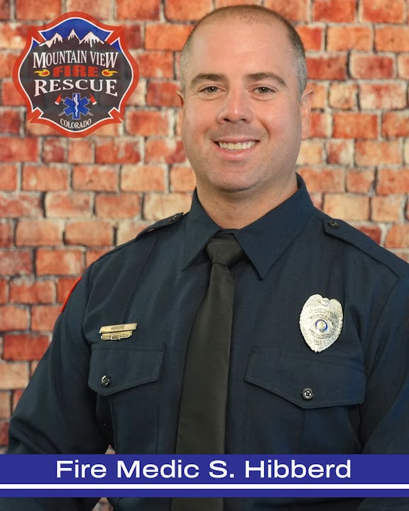 A firefighter in uniform with a Mountain View Fire Rescue badge, smiling, in front of a brick wall. Text: "Fire Medic S. Hibberd".