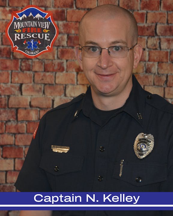 A firefighter in uniform in front of a brick wall with a Mountain View Fire Rescue logo, labeled "Captain N. Kelley."
