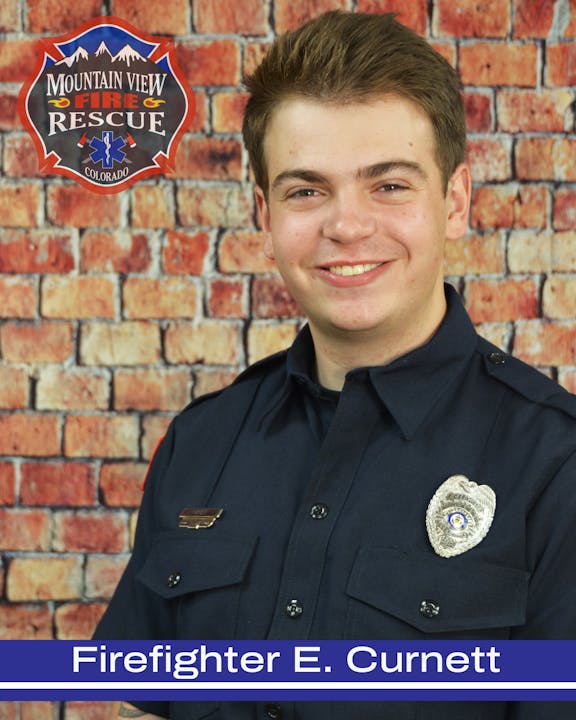 A smiling person in firefighter uniform with a badge, in front of a brick wall background, with text indicating they are a firefighter.