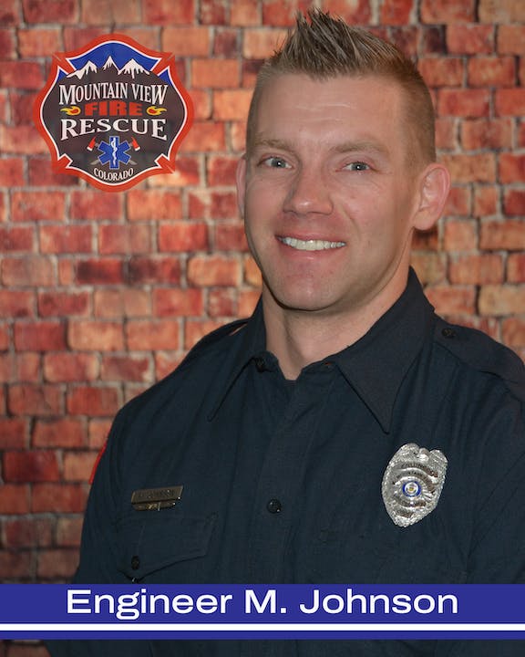 A smiling man in a firefighter's uniform with badge. "Mountain View Fire Rescue Colorado" and "Engineer M. Johnson" text. Brick background.