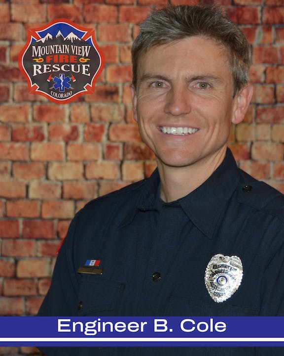 A smiling firefighter in uniform with a badge, standing before a brick wall, with a logo "Mountain View Fire & Rescue Colorado."