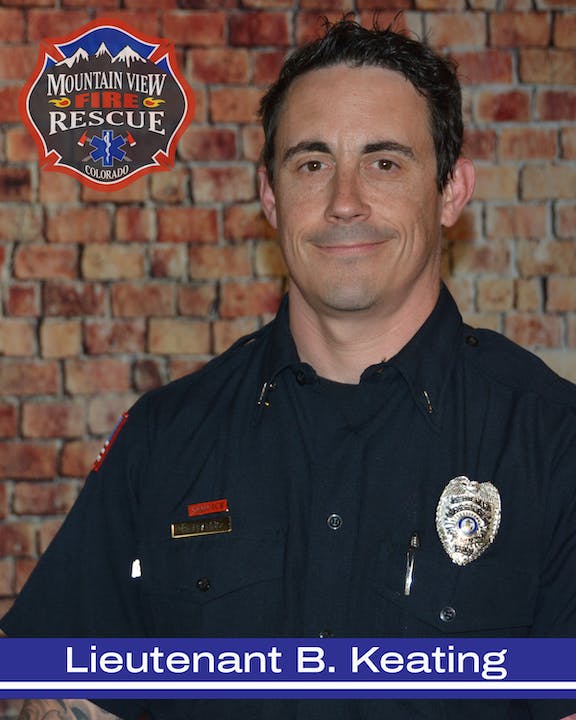 A smiling individual in firefighter uniform with a badge that reads "Lieutenant." Brick background and fire department logo visible.