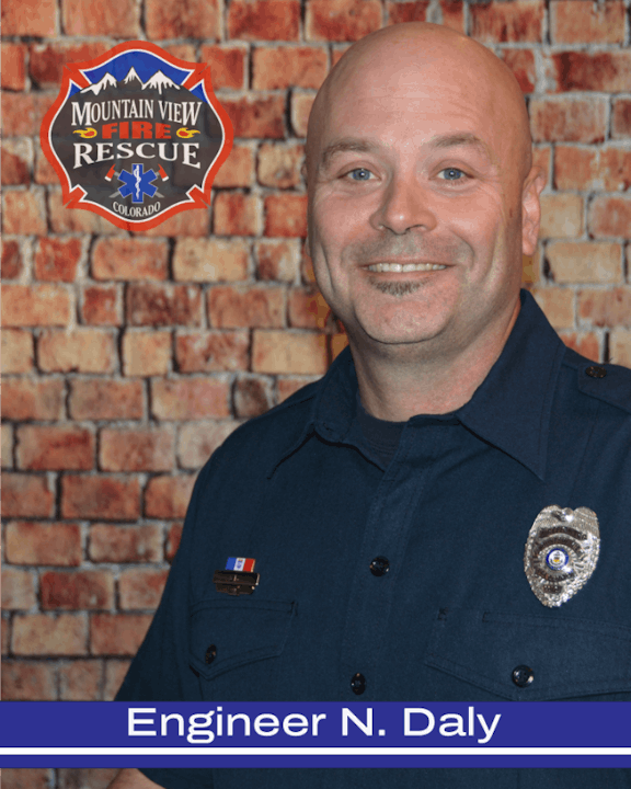 A smiling firefighter in uniform with a name tag and fire department logo.