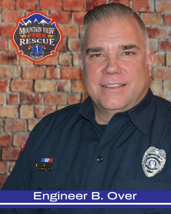 A firefighter in uniform with a badge, in front of a brick wall and a Mountain View Fire Rescue logo.