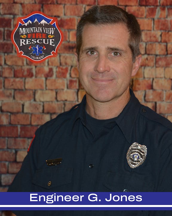 A man in a firefighter uniform with a badge, in front of a brick wall with a "Mountain View Fire Rescue Colorado" emblem.