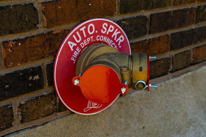 A fire department connection (FDC) for sprinklers mounted on a brick wall.