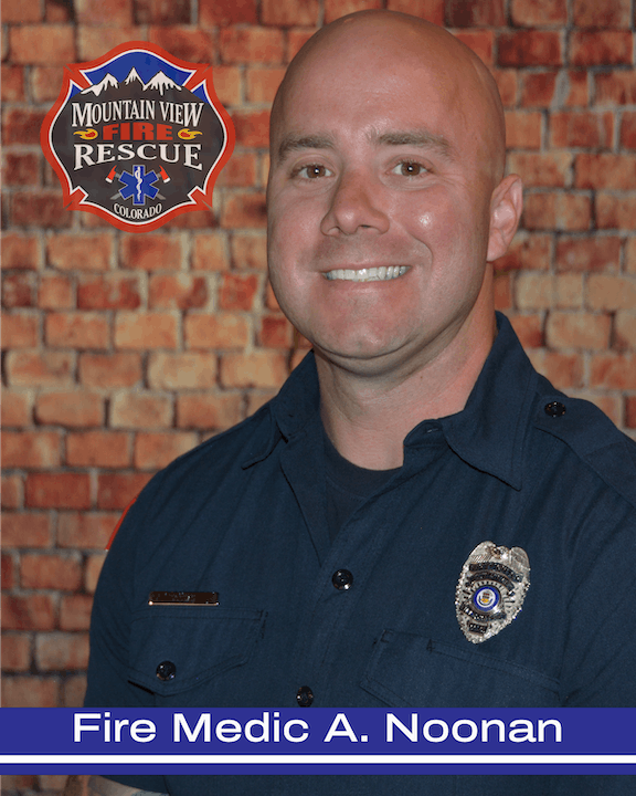 A smiling firefighter in uniform in front of a brick wall, with a Mountain View Fire Rescue patch logo.