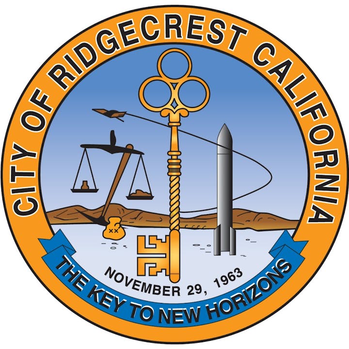 Seal of Ridgecrest, California with a key, scale, rocket, plane, mountains, and date "November 29, 1963." Text: "The Key to New Horizons."