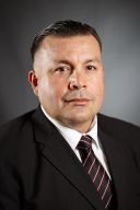 A man in a suit and tie, posing for a portrait against a gray background.
