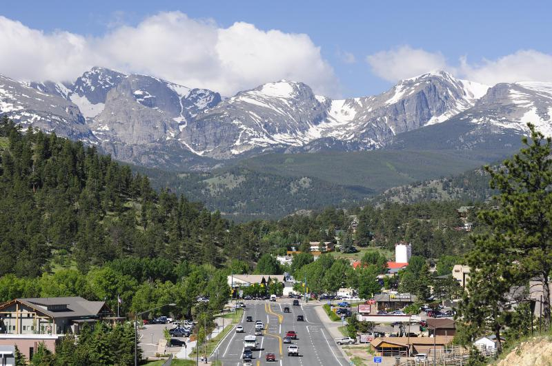 A town in a valley with a main road, surrounded by forested hills and snow-capped mountains in the background.