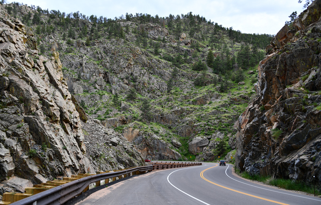 A winding road through a rocky mountain landscape with green vegetation and a clear sky.
